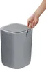 A hand is shown opening the lid of a gray trash can. Podgląd zdjęcia produktu