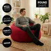 A man is sitting on a red beanbag chair in a living room. Voir les images du produit