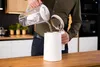 A person is pouring filtered water from a pitcher into a white electric kettle. Produktbild-Vorschau