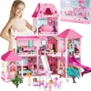 A young girl stands behind a large pink dollhouse, which is set up with furniture, dolls, and accessories. The dollhouse is elaborate and multi-story, featuring a slide, balconies, and various rooms. A box for the dollhouse is visible in the upper right co Voir les images du produit
