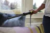 A person is using a steam cleaner attachment to clean a sofa cushion in a well-lit room. Produktbild-Vorschau