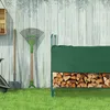A green firewood rack with a cover, filled with firewood, stands against a wooden fence. Garden tools like a shovel and rake are leaning against the fence. Náhled obrázku produktu