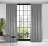A pair of gray velvet curtains are shown hanging in front of a large window with a grid pattern. There are two small side tables with decorative items next to the curtains. Produktbild-Vorschau
