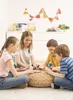 Four children are sitting on the floor around a round, woven pouf, playing a card game. Voir les images du produit