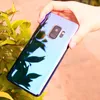 A hand holding a smartphone with a reflective, color-changing case, with green leaves in the foreground. Produktbild-Vorschau