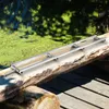 A portable sawmill guide system is set up on a large log, with a body of water covered in green algae in the background. Produktbild-Vorschau