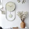 A minimalist pendulum wall clock is displayed on a white wall, with decorative branches and a vase of dried flowers nearby. Voir les images du produit