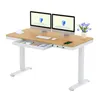 A white electric standing desk with a wood-tone desktop, dual monitors, a keyboard, a mouse, a cup, a drawer, and a phone charging. Produktbild-Vorschau