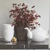 A white teapot and two white cups are arranged on a dark marble countertop next to a potted plant with dark red leaves and some sugar cubes. Produktbild-Vorschau