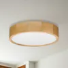 A round, modern ceiling light with a wooden frame and a white diffuser, mounted on a white ceiling. Produktbild-Vorschau