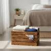 A wooden crate filled with folded clothes is placed on the floor in front of a bed. Anteprima dell’immagine prodotto