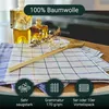 A close-up view of kitchen towels with a wooden spoon and bottles of oil in the background. Produktbild-Vorschau