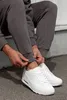 A person is adjusting the cuff of their grey sweatpants while wearing white sneakers. Produktbild-Vorschau