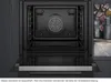 An open built-in oven with a view of the interior and a glimpse of a cookbook and bottle on a counter to the right. Produktbild-Vorschau