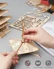 A person's hands are assembling a wooden model of a five-story pagoda, with various wooden pieces and instructions visible on a gray surface. Voir les images du produit
