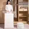 A woman is demonstrating how to use a vacuum storage bag in a closet setting. There are clothes hanging in the background and a compressed bag on the floor. Produktbild-Vorschau