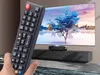A hand holding a remote control in front of a large screen displaying a colorful landscape. Náhled obrázku produktu