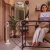A woman is working at a desk with a laptop, while a tower fan is placed in the background. Podgląd zdjęcia produktu