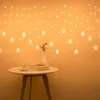 A string of star-shaped LED lights hangs against an orange wall, with a small table in the foreground holding a book and a cup. Produktbild-Vorschau