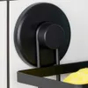 A close-up of a black metal shower caddy attached to a tiled wall with suction cups. A yellow sponge is visible inside the caddy. Podgląd zdjęcia produktu