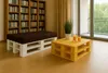 A living room with a bookshelf, a pallet bench with a cushion, and a pallet coffee table with drinks and a plant. Produktbild-Vorschau