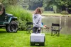 A person stands next to a portable refrigerator and a Jeep, with a lake and trees in the background. Náhľad obrázku produktu