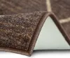 A close-up view of a brown rug with a beige checkered pattern, showing the texture and edge. Produktbild-Vorschau
