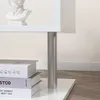 Close-up of a white side table with a silver cylindrical leg, showing stacked books on the lower shelf. Produktbild-Vorschau