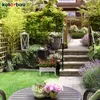A lush garden scene with a pathway leading up stone steps, flanked by lavender and other plants. A table with potted plants is in the foreground. Produktbild-Vorschau
