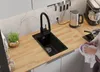 A modern kitchen scene with a black sink and faucet, a kettle, a stand mixer, and a person washing a bowl. Produktbild-Vorschau