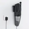 A black handheld vacuum cleaner is mounted on a white wall next to a white electrical socket with a black plug. Produktbild-Vorschau
