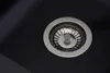 A close-up view of a black kitchen sink drain with a silver strainer. Produktbild-Vorschau