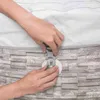 Hands are shown securing a buckle on a cover, likely for a hot tub or spa, against a stone-like textured surface. Produktbild-Vorschau