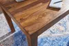 A close-up of a wooden dining table with a patterned rug underneath. Náhľad obrázku produktu