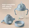 A collection of baby feeding accessories, including a sippy cup with handles and a straw, a separate lid, and a base. Produktbild-Vorschau
