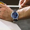 A person's arm wearing a watch is shown while measuring something with a tape measure. Produktbild-Vorschau