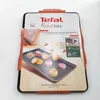 The image shows the packaging of a Tefal baking tray, with a picture of macarons on the tray. Voir les images du produit