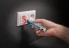 A hand is using a voltage tester to check an electrical outlet. Voir les images du produit