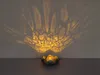 A solar-powered lantern with a lotus-shaped base, casting intricate shadows on a wall. Produktbild-Vorschau