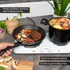 A hand is shown holding the handle of a frying pan containing steak and vegetables, placed on a white electric double hot plate. A pot of pasta and vegetables is on the other burner. The scene is set on a kitchen counter with plants and a woven basket in t Produktbild-Vorschau