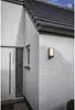 Exterior view of a modern house with a white brick wall, a white door, a small window, and a dark gray roof. An anthracite LED outdoor wall light with a motion detector is mounted on the wall. Anteprima dell’immagine prodotto