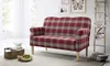 A red plaid sofa is shown in a living room setting with decorative items. Produktbild-Vorschau