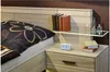 A bedside table with a digital clock and books next to a bed with a floral patterned pillow. Anteprima dell’immagine prodotto