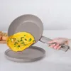 A hand is holding a frying pan with an omelet in it, over a plate. Produktbild-Vorschau
