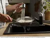A person is rinsing rice in a colander under a kitchen faucet. Produktbild-Vorschau