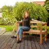 A woman sits on a wooden garden bench in a lush garden setting. Produktbild-Vorschau