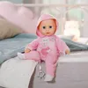 A baby doll is sitting on a bed with pillows and a blanket. Náhled obrázku produktu