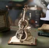 A detailed wooden model of a cello with intricate gears and a flower decoration, placed on an open book. Voir les images du produit