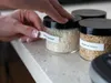 A person is labeling jars of rice on a countertop. Produktbild-Vorschau