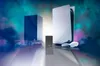 A PlayStation 5 console and controller are displayed alongside a blue rectangular object and a small gray external hard drive, set against a backdrop of colorful smoke or mist. Produktbild-Vorschau